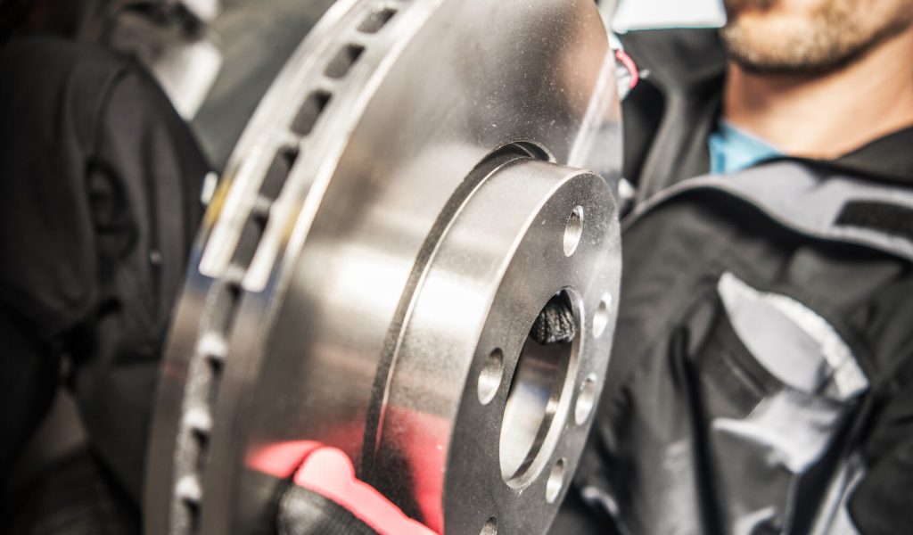 Caucasian Male Technician Working At Auto Repair Shop Replacing Disc In Car Braking System.