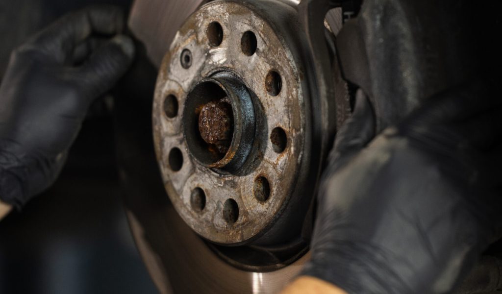 Mechanic at service station checks the brake and steering systems. Strong man checks for wear in running gear and steering components. Service operator in overalls. Car moves on lift.